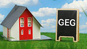 Symbolbild: Links steht ein Haus, rechts eine Schiefertafel mit der Aufschrift "GEG".