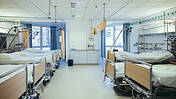 Blick in ein Patientenzimmer im Krankenhaus, man sieht sechs Betten, die eng aneinander stehen.