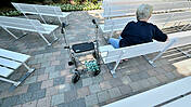Symbolfoto: Eine ältere Dame sitzt alleine auf der Parkbank, neben ihr steht ein Rollator.