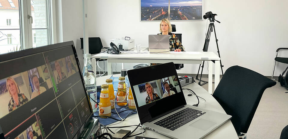 Verena BEntele an ihrem Schreibtisch, im Vordergrund sieht man die aufgebaute Streaming-Technik wie Kamera, Notebooks.