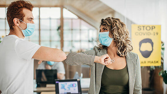 Mann und Frau mit Schutzmasken Grüße mit Ellenbogen im Büro