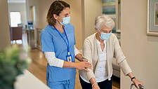 Weibliche Pflegekraft hilft Seniorin beim Gehen im Pflegeheim