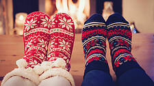 Vier Paar Füße in Weihnachtssocken in der Nähe des Kamin zum Füße aufwärmen.