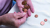 Hände einer alten Frau über einem Tisch, zählt eine Hand voll Münzen