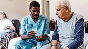Pfleger gibt Medizikamente an einen älteren Mann