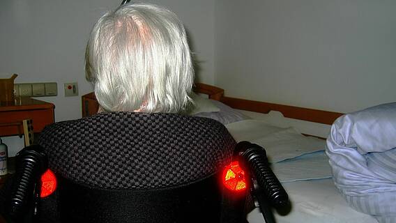 Frau im Rollstuhl vor einem Bett