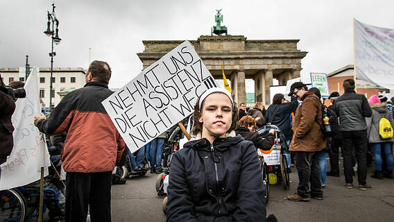 Demo-Teilnehmerin mit Schild: Nehmt uns die Assistenzen nicht weg