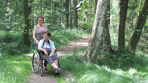 Zwei Frauen beim Wandern im Wald, eine davon sitzt im Rollstuhl