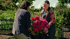 Auf dem Foto ist eine Szene aus dem Werbefilm der Deutschen Rentenversicherung zur medizinischen Rehabilitation zu sehen, bei dem zwei Frauen einen Blumentopf gemeinsam hochheben.