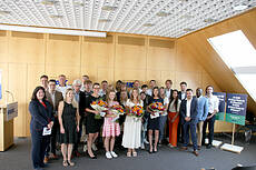 Auf dem Foto sieht man die Absolventinnen des VdK Bayern (vier junge Frauen, die einen Blumenstrauß in der Hand halten) mit ihren AUsbilderinnen und AUsbildern und Personalverantwortlichen sowie den neuen Auszubildenenden in einem Sitzungssaal des VdK Bayern.