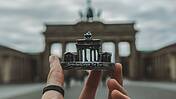 Hand hält kleine Magnetabbildung des Brandenburger Tors vor das Originalbauwerk.