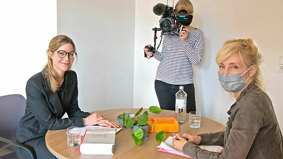 An einem runden Tisch sitzen sich gegenüber VdK-Juristin Kathrin Brückner und NDR-Reporterin Susann Kowatsch. Dazwischen im Hintergrund die NDR-Kamerafrau mit Kamera.