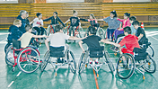 Ein Gruppe von Rollstuhlsportlern bilden in einer Halle einen Kreis.