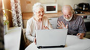 Ein älteres Ehepaar sitzt vor einem Laptop in der Küche beim Video-Chat