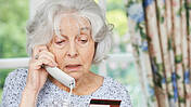 Eine Seniorin mit Karte in der Hand telefoniert.