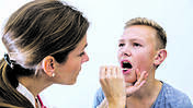 Eine Ärztin untersucht die Mundhöhle eines Jugendlichen.