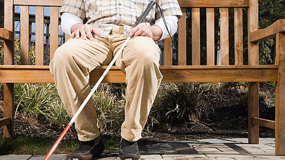Symbolfoto: Ein Mann mit einem Blindenstock sitzt auf einer Bank.