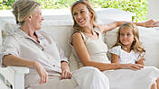 Symbolfoto: Oma, Tochter und Enkelin sitzen gemeinsam auf einer Couch