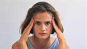 Symbolfoto: Eine Frau massiert sich die Schläfen, als hätte sie Kopfschmerzen
