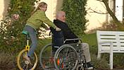 Symbolfoto: Ein Mädchen mit einem Einrad schiebt einen Senior im Rollstuhl