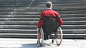 Symbolfoto: Ein Mann im Rollstuhl steht am Fuß einer Treppe