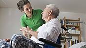 Symbolfoto: Angehörige oder Pflegekraft beugt sich über einen Senior im Rollstuhl