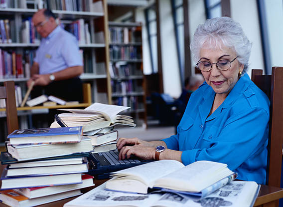 Symbolfoto: Eine alte Dame liest in einer Bibliothek ein Buch.