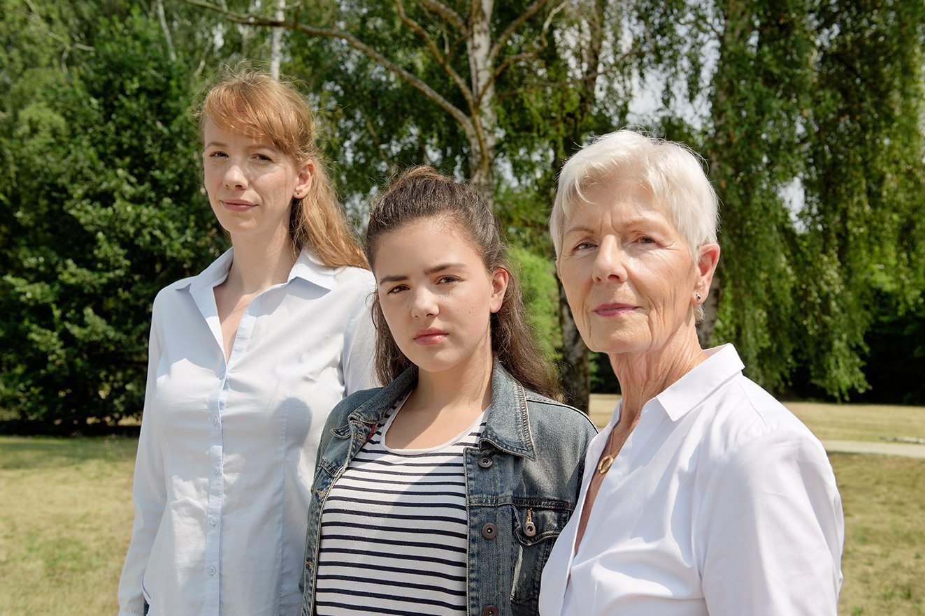 Drei Frauen blicken gemeinsam ernst in die Kamera: Eine j&uuml;ngere, eine Teenagerin und eine &auml;ltere Frau.